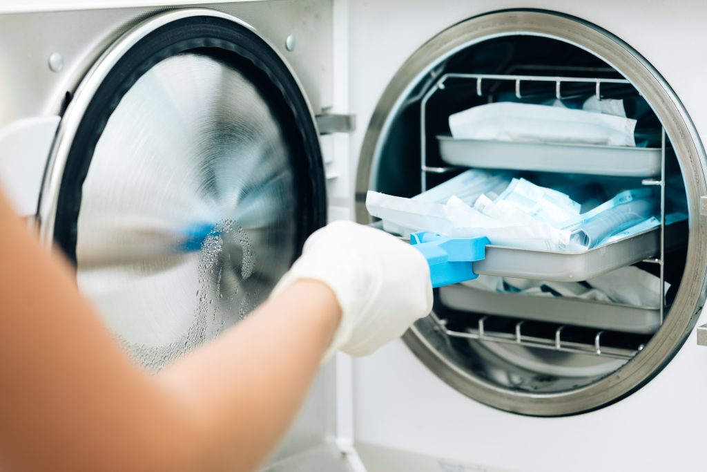 Nurse putting instruments in special craft paper bags into autoclave for processing. Modern laboratory equipment. Tools sterilization, bacterial purification and disinfection in dental clinic.